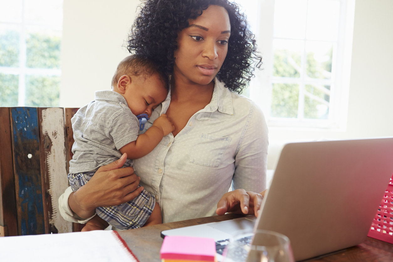 a mother holds her baby while working on a laptop