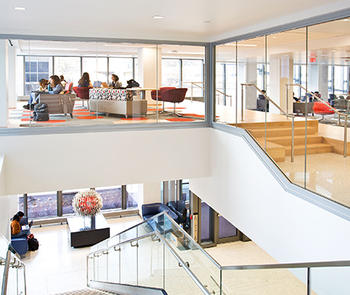an interior photo of an office with glass railings along a staircase and glass walls between a hallway and meeting rooms